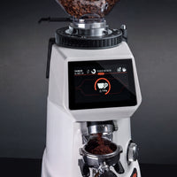 A white and black coffee grinder with a digital touch screen displaying coffee bean processing metrics, shown with coffee beans in the hopper and ground coffee falling into a portafilter against a dark gray background.